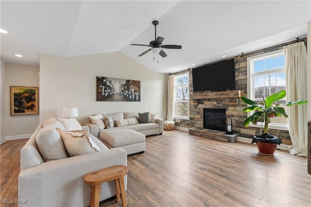 living room with lofted ceiling, hardwood / wood-style floors, a stone fireplace, and ceiling fan