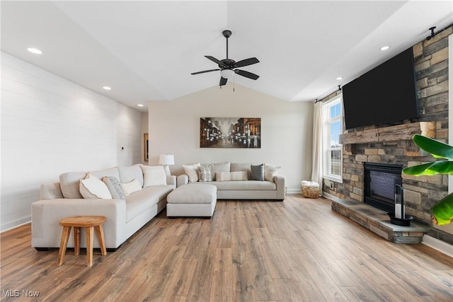 living room with ceiling fan, wood-type flooring, a stone fireplace, and vaulted ceiling