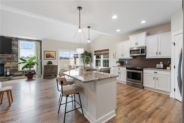 kitchen featuring decorative light fixtures, stainless steel appliances, white cabinets, and a center island with sink