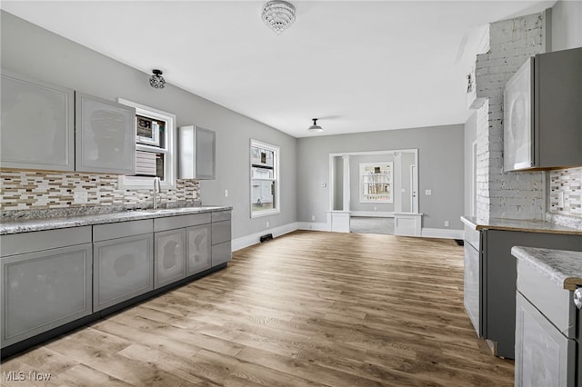 kitchen with gray cabinets, tasteful backsplash, sink, and light wood-type flooring