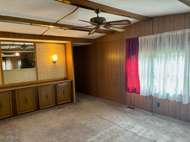 carpeted spare room featuring ceiling fan, beam ceiling, and wood walls