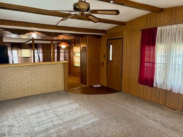 carpeted empty room with vaulted ceiling with beams, ceiling fan, and wood walls