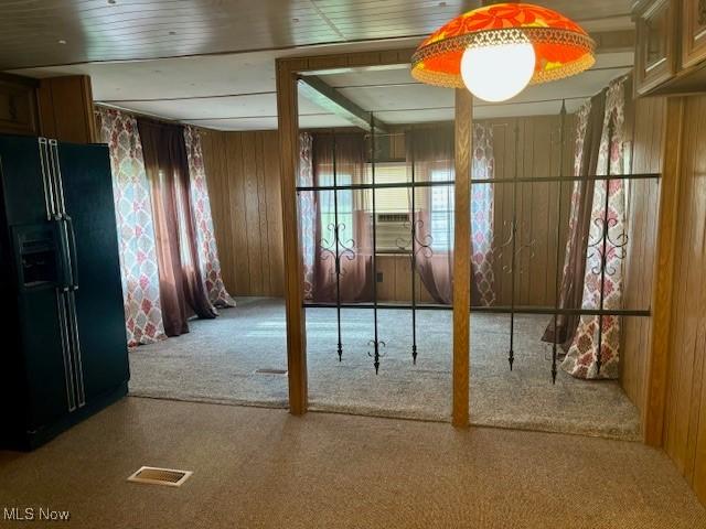 interior space with carpet flooring, wooden walls, and black fridge