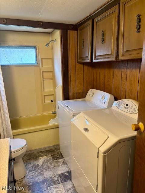 laundry area with washing machine and clothes dryer and wood walls