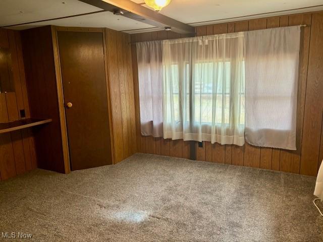 spare room with beam ceiling, wooden walls, and carpet flooring