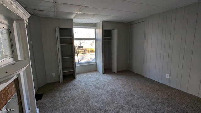 unfurnished room with carpet, a drop ceiling, and wood walls