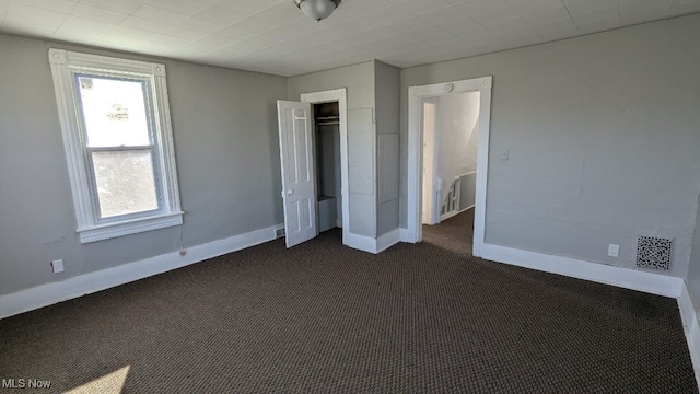 unfurnished bedroom with dark carpet and a closet