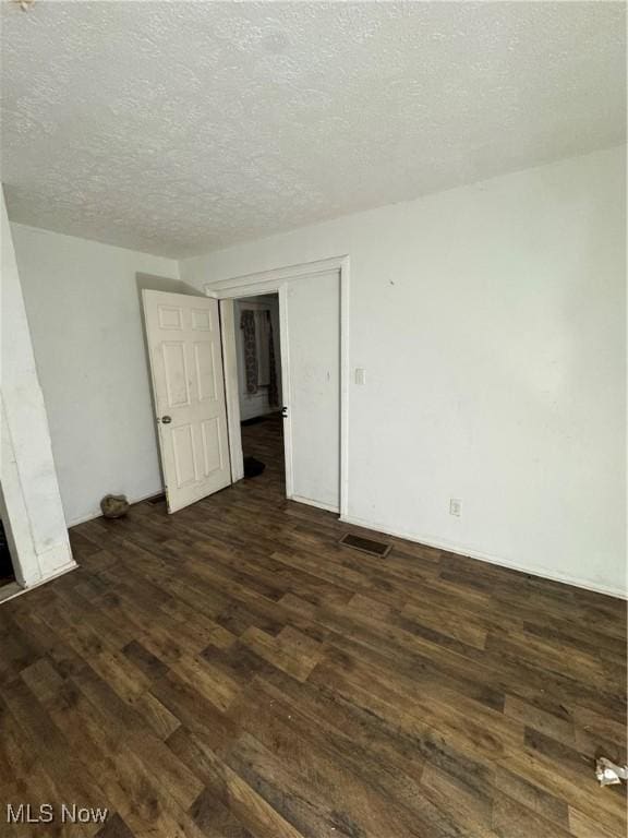 spare room featuring a textured ceiling and dark hardwood / wood-style flooring