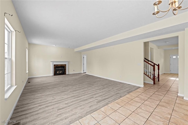 unfurnished living room featuring a premium fireplace, an inviting chandelier, and light wood-type flooring