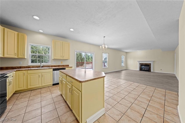 kitchen with a kitchen island, decorative light fixtures, sink, stainless steel dishwasher, and light tile patterned floors