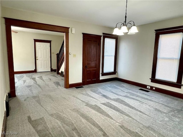 spare room featuring light carpet and a notable chandelier