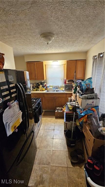 kitchen with black fridge, gas range, sink, and a textured ceiling