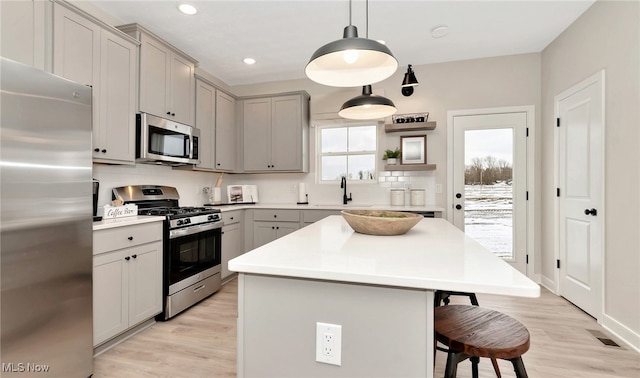 kitchen with a breakfast bar, appliances with stainless steel finishes, gray cabinets, a kitchen island, and pendant lighting