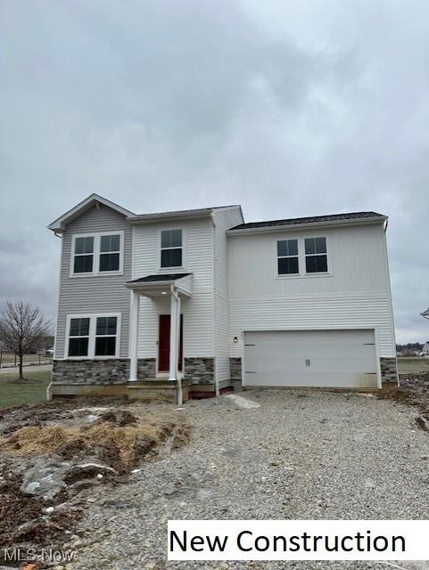 traditional home featuring stone siding, a garage, and gravel driveway