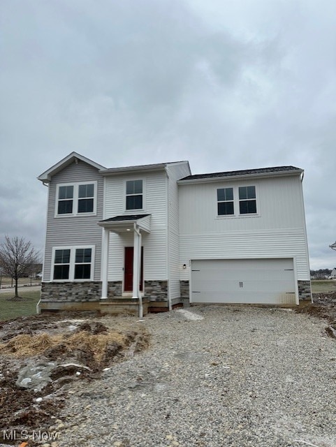 traditional home with stone siding, a garage, and gravel driveway