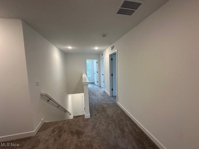 hallway featuring visible vents, baseboards, an upstairs landing, and carpet flooring