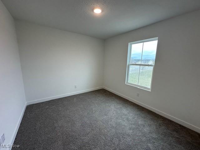 empty room with baseboards and dark colored carpet