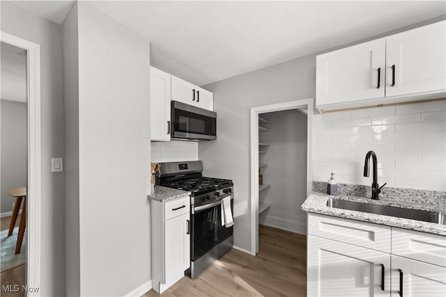 kitchen with sink, stainless steel appliances, light stone counters, white cabinets, and light wood-type flooring