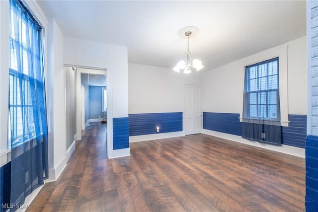 spare room featuring dark wood-type flooring, a notable chandelier, and a wealth of natural light