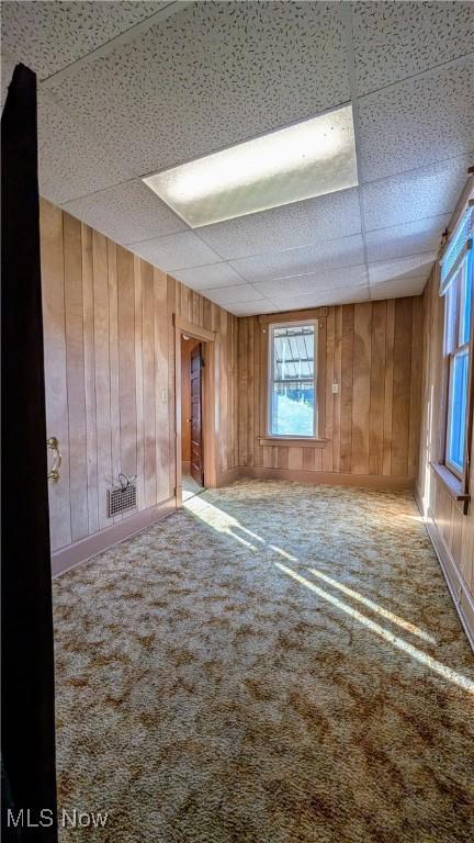 carpeted empty room featuring a paneled ceiling and wood walls