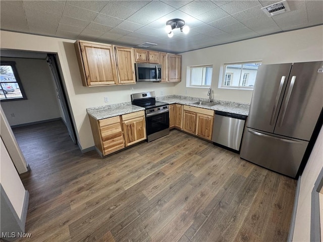 kitchen with light stone countertops, appliances with stainless steel finishes, sink, and dark hardwood / wood-style flooring