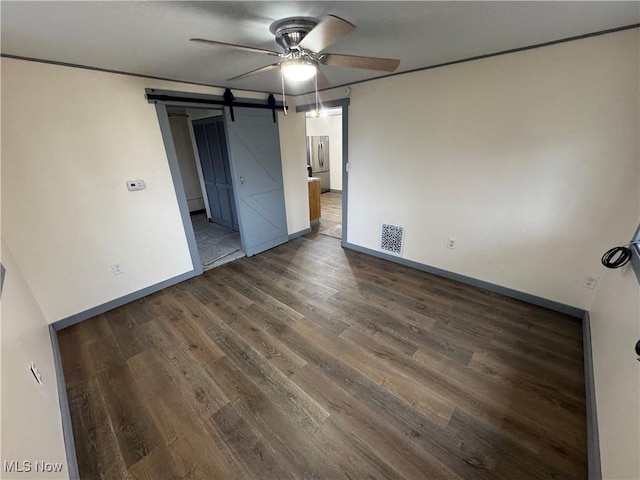 unfurnished bedroom with ceiling fan, a barn door, stainless steel fridge, and dark hardwood / wood-style flooring