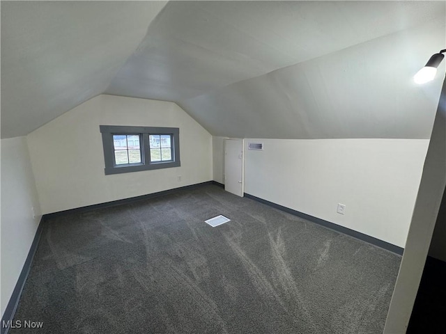 bonus room with vaulted ceiling and dark colored carpet