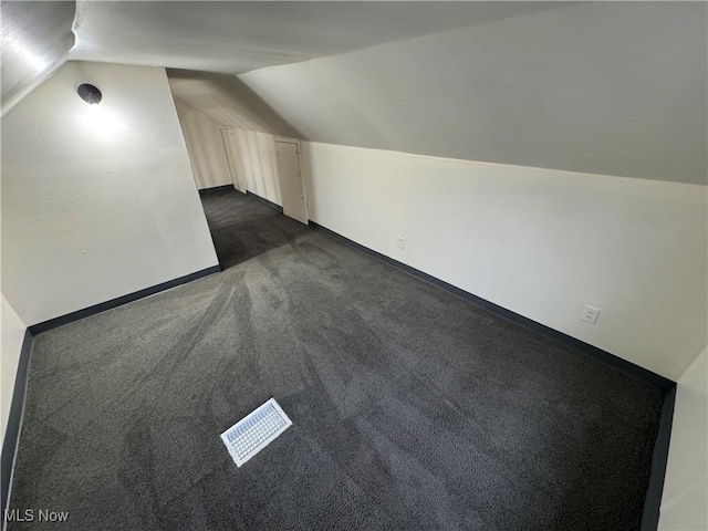 additional living space featuring dark carpet and vaulted ceiling