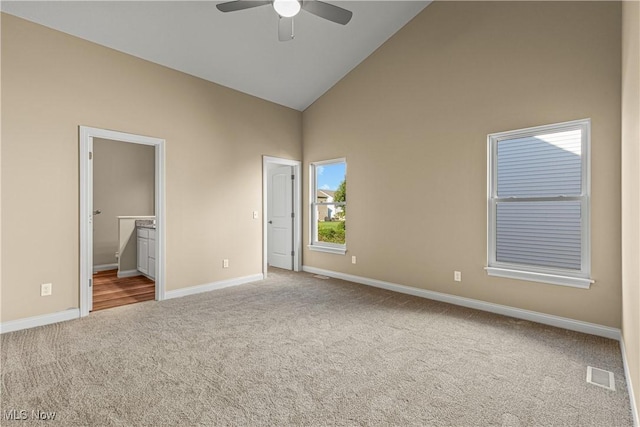 unfurnished bedroom featuring ceiling fan, ensuite bathroom, high vaulted ceiling, and light carpet