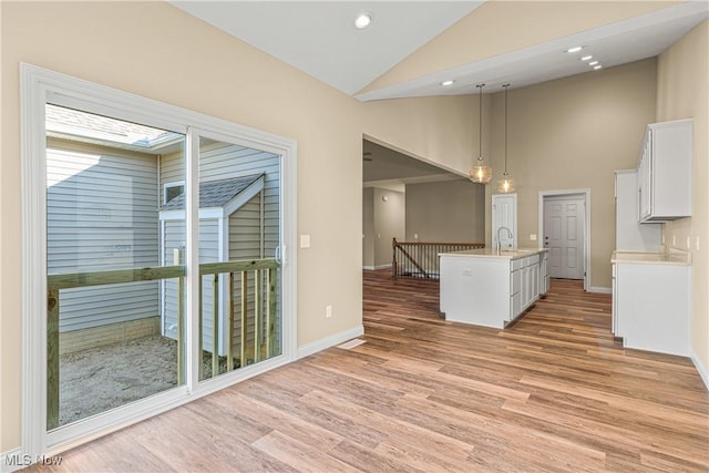 kitchen featuring sink, hanging light fixtures, light wood-type flooring, a center island with sink, and white cabinets