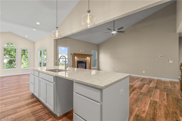 kitchen featuring sink, light stone counters, an island with sink, white cabinets, and decorative light fixtures