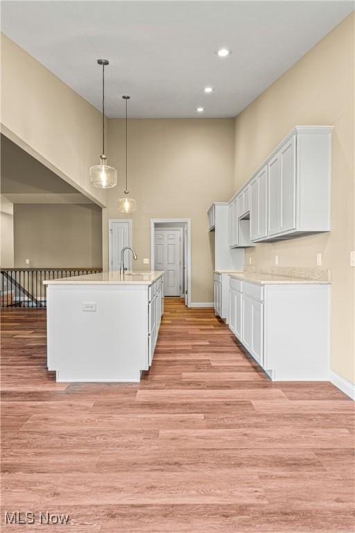 kitchen featuring sink, light hardwood / wood-style flooring, white cabinetry, an island with sink, and decorative light fixtures