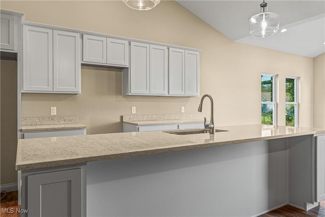 kitchen featuring pendant lighting, lofted ceiling, sink, and light stone counters