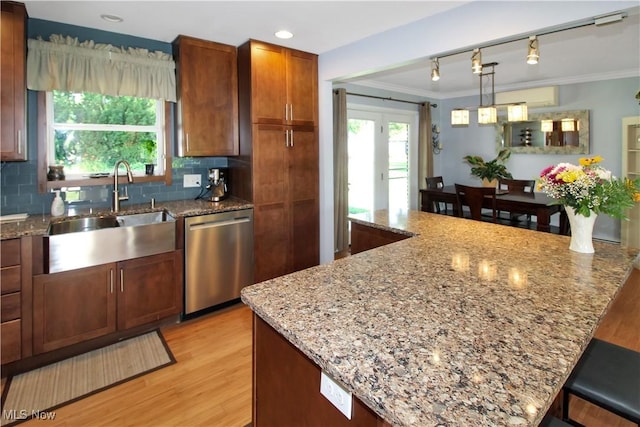 kitchen featuring a kitchen bar, sink, hanging light fixtures, stainless steel dishwasher, and light stone countertops