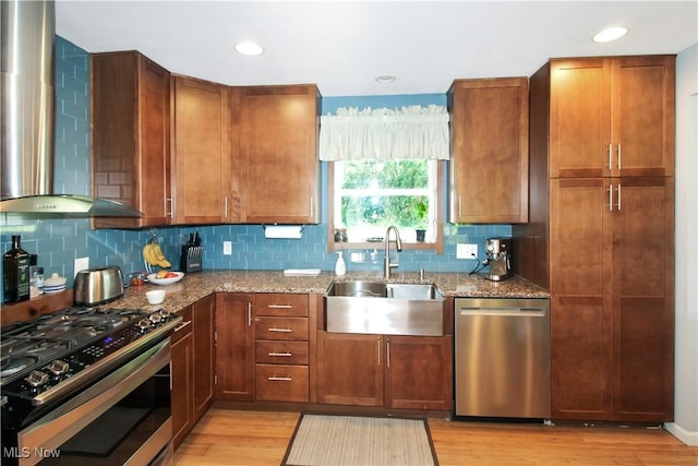 kitchen featuring wall chimney exhaust hood, sink, appliances with stainless steel finishes, light stone countertops, and light hardwood / wood-style floors