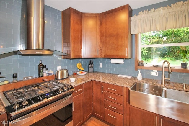 kitchen with sink, light stone counters, tasteful backsplash, stainless steel gas range oven, and wall chimney exhaust hood