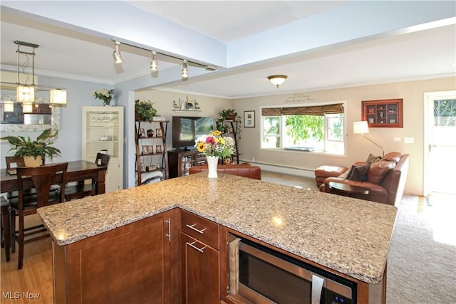 kitchen with hanging light fixtures, ornamental molding, a center island, light colored carpet, and light stone counters