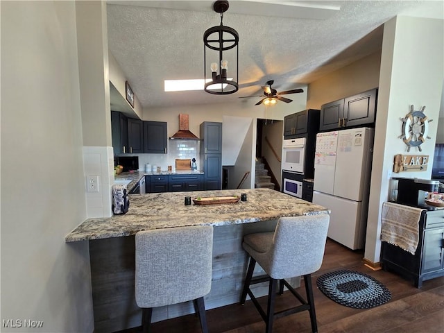 kitchen featuring pendant lighting, white appliances, a breakfast bar area, custom exhaust hood, and kitchen peninsula