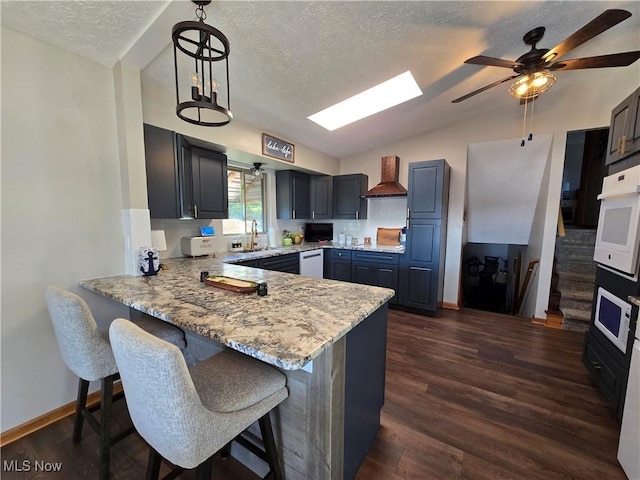 kitchen with custom range hood, vaulted ceiling with skylight, oven, and decorative light fixtures