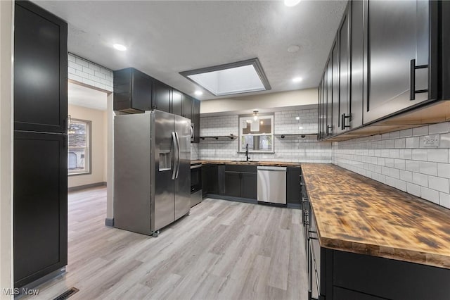 kitchen with sink, butcher block counters, backsplash, stainless steel appliances, and light hardwood / wood-style floors