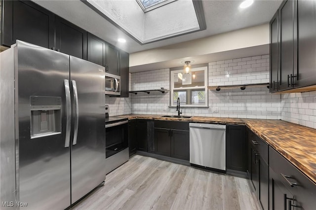 kitchen with appliances with stainless steel finishes, sink, light hardwood / wood-style floors, and wooden counters