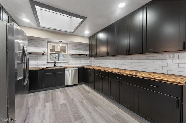 kitchen with tasteful backsplash, butcher block counters, sink, stainless steel appliances, and light hardwood / wood-style flooring