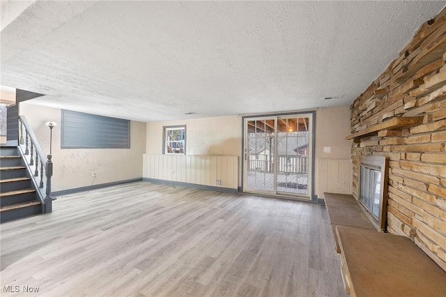 unfurnished living room featuring a wealth of natural light, light hardwood / wood-style floors, a large fireplace, and a textured ceiling