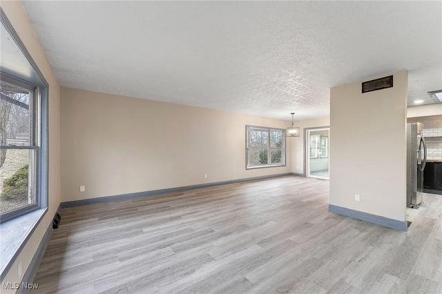 unfurnished living room with an inviting chandelier, light hardwood / wood-style floors, and a textured ceiling