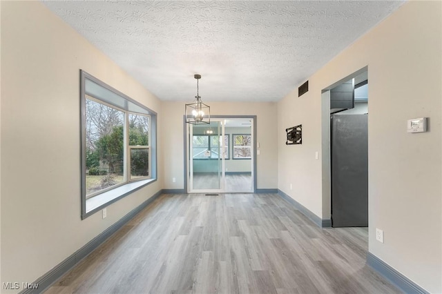 unfurnished dining area with a chandelier, a textured ceiling, and light wood-type flooring