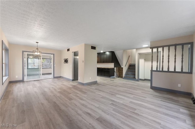 unfurnished living room with elevator, an inviting chandelier, a textured ceiling, and light wood-type flooring