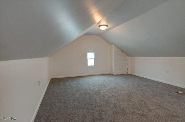 bonus room with lofted ceiling and dark colored carpet