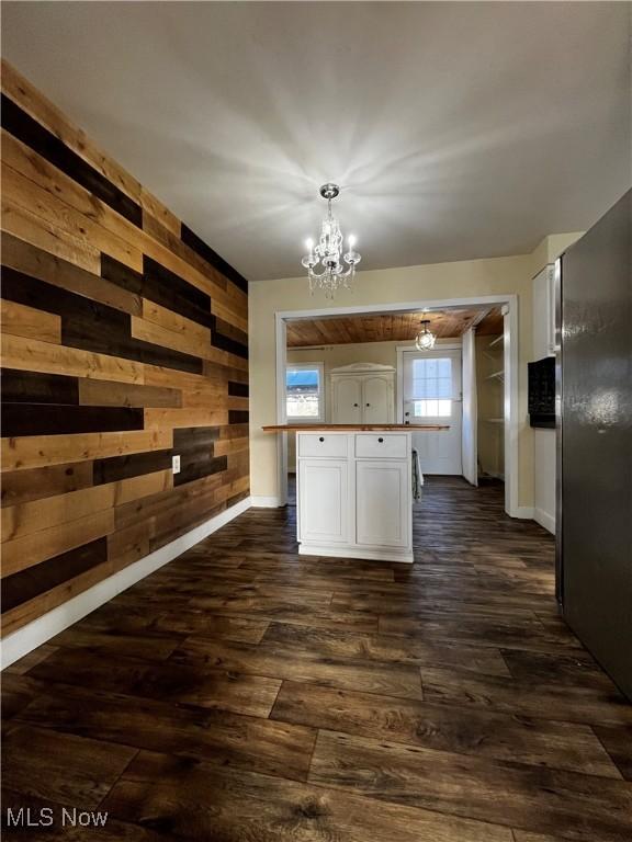 kitchen featuring pendant lighting, dark hardwood / wood-style floors, a center island with sink, a chandelier, and wood walls