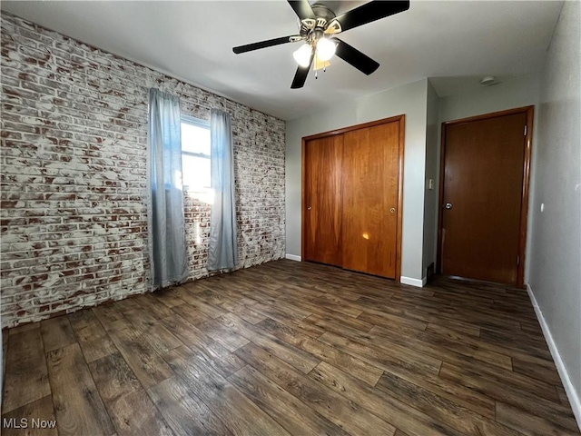 unfurnished bedroom featuring ceiling fan, brick wall, dark hardwood / wood-style floors, and a closet