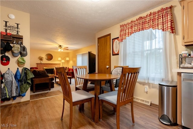 dining area with ceiling fan, a brick fireplace, a textured ceiling, and light wood-type flooring